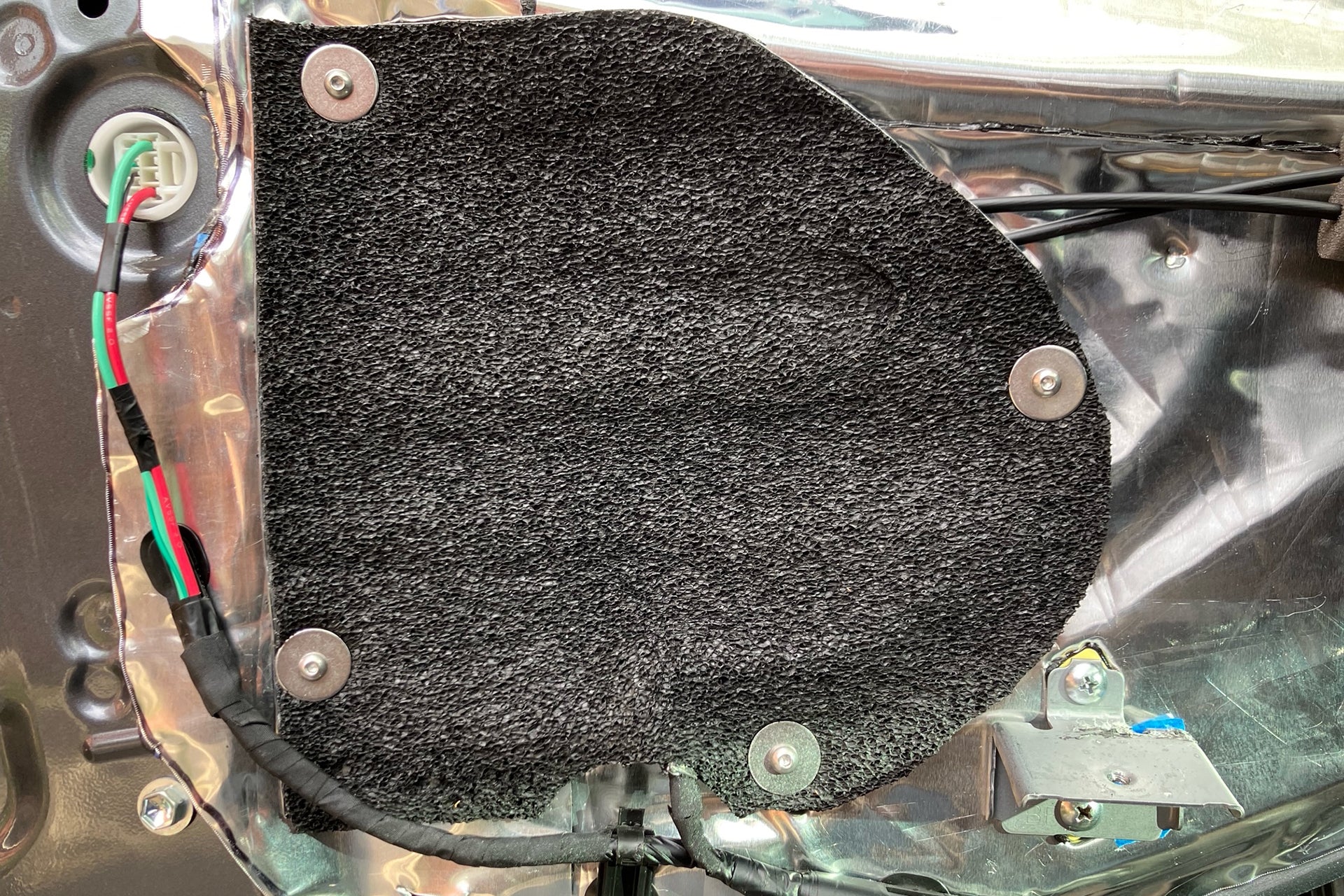 ResoNix Barrier being used to seal up access holes on the inner door skin of a vehicle. The inner door skin also has ResoNix CLD Squares sound deadener mats applied.