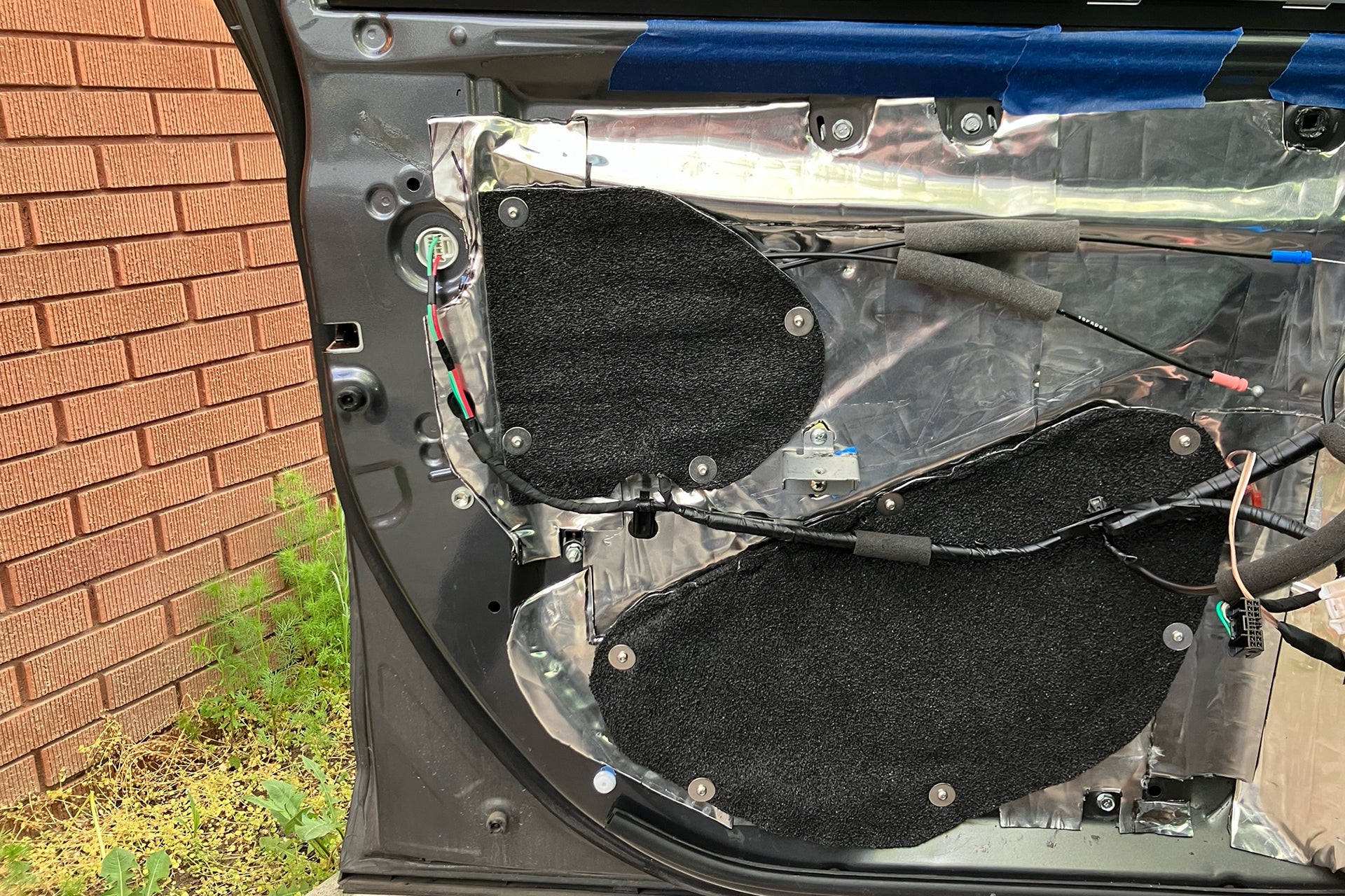 ResoNix Barrier being used to seal up access holes on the inner door skin of a vehicle. The inner door skin also has ResoNix CLD Squares sound deadener mats applied.